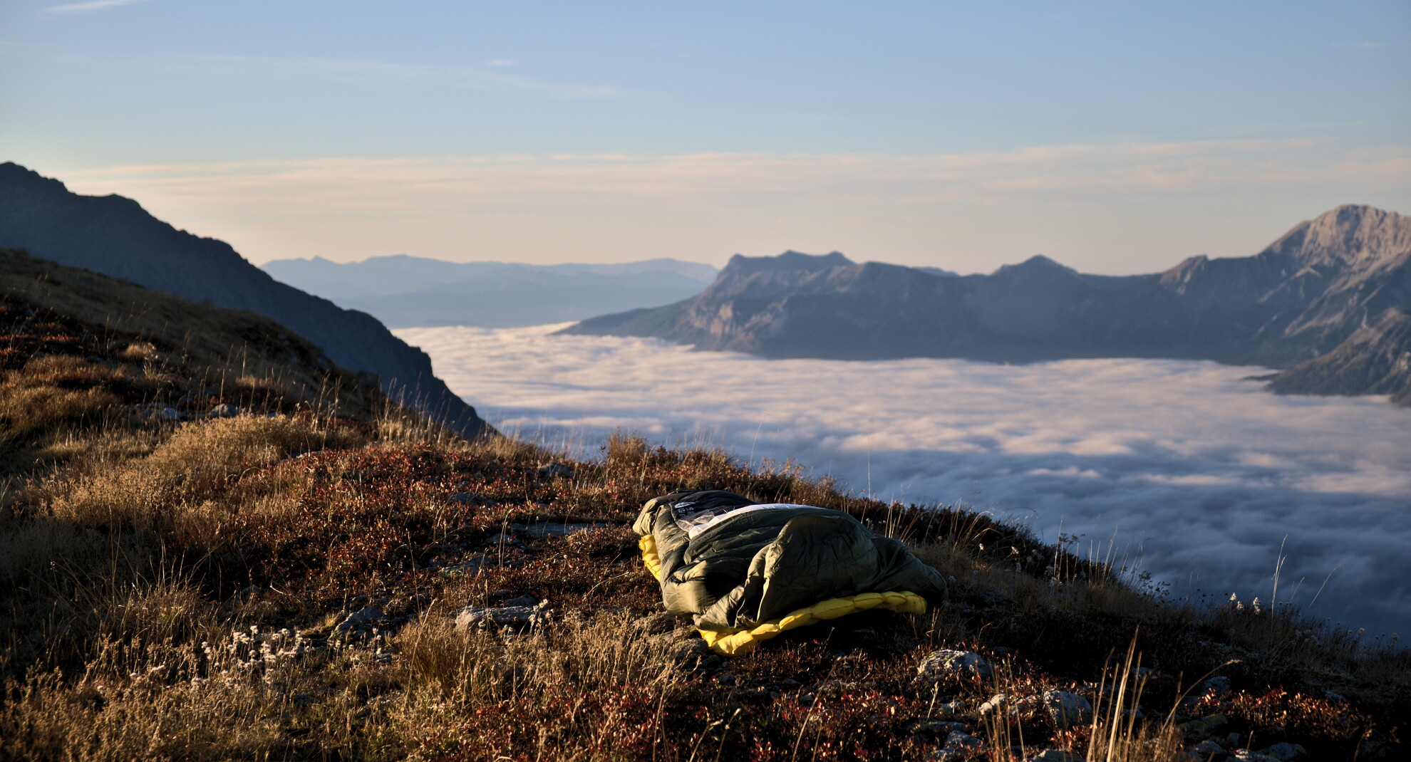 Sleeping bag laid out on a grassy shoulder above a sea of clouds